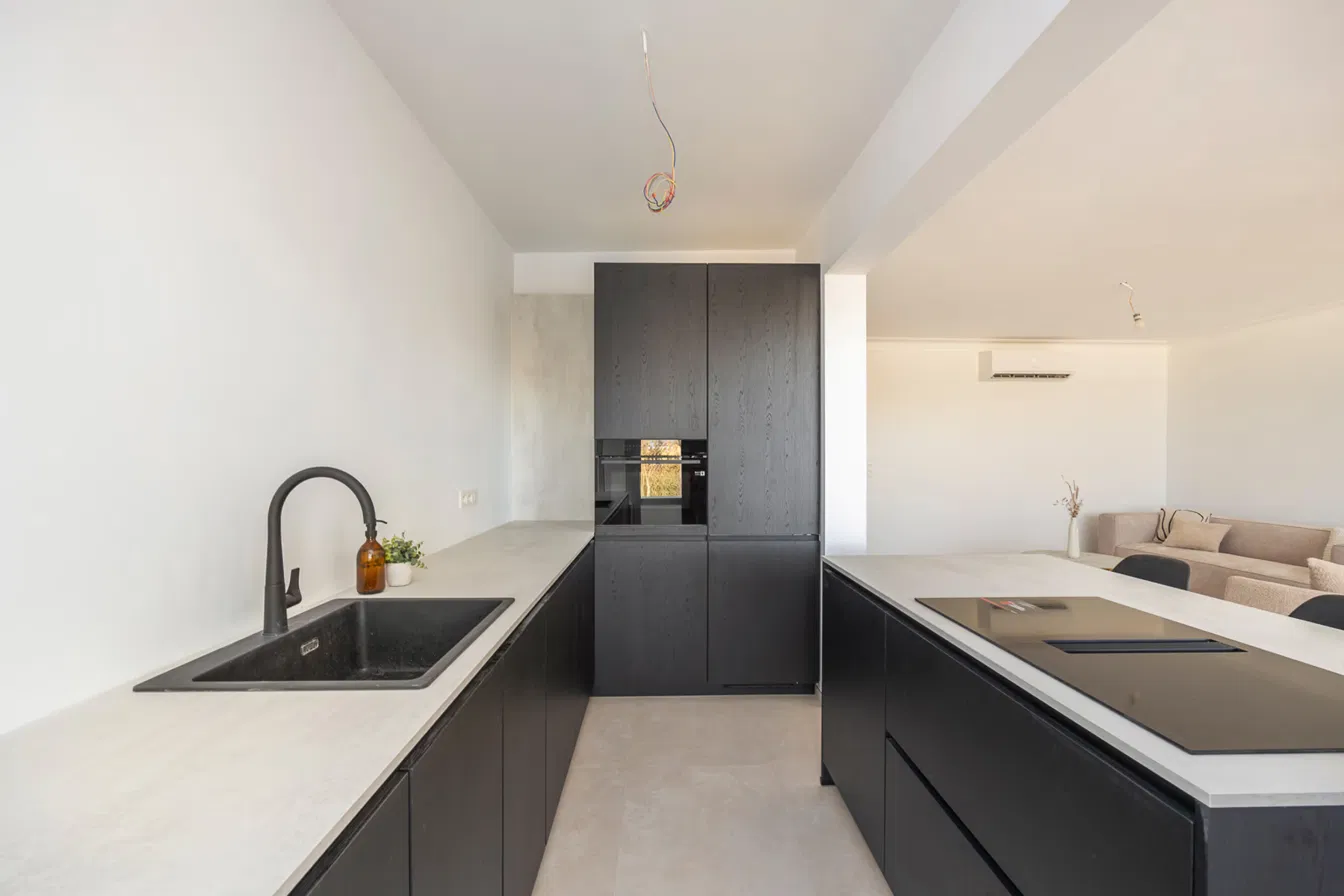 Moderne keuken met zwarte houten kasten, licht werkblad, inbouwoven en kookeiland met inductiekookplaat in Residentie Den Berm in Mortsel