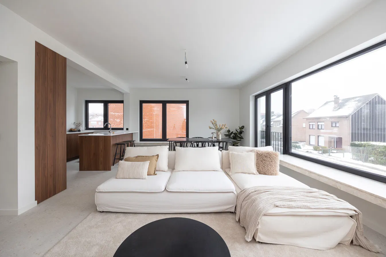 Ruime leefruimte met hoekzetel, groot raam met vensterbank en open keuken in notenhout in gerenoveerd appartement aan de Heislagsebaan 198 in Brasschaat
