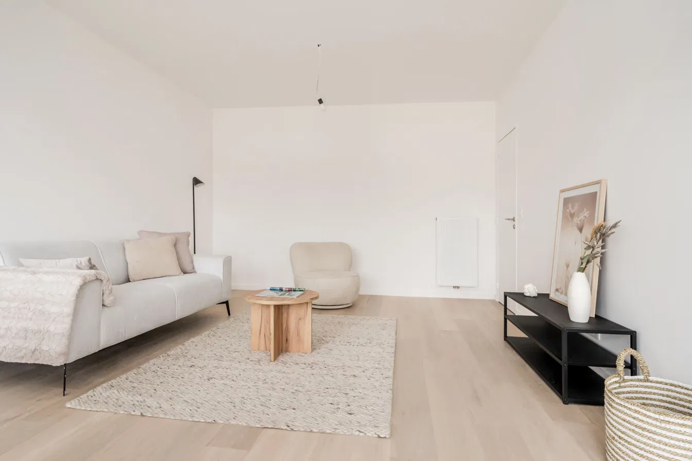 Zithoek met lichte zetel, fauteuil en houten salontafel op een lichte parketvloer in appartement aan de Lambert Briesstraat in Berchem