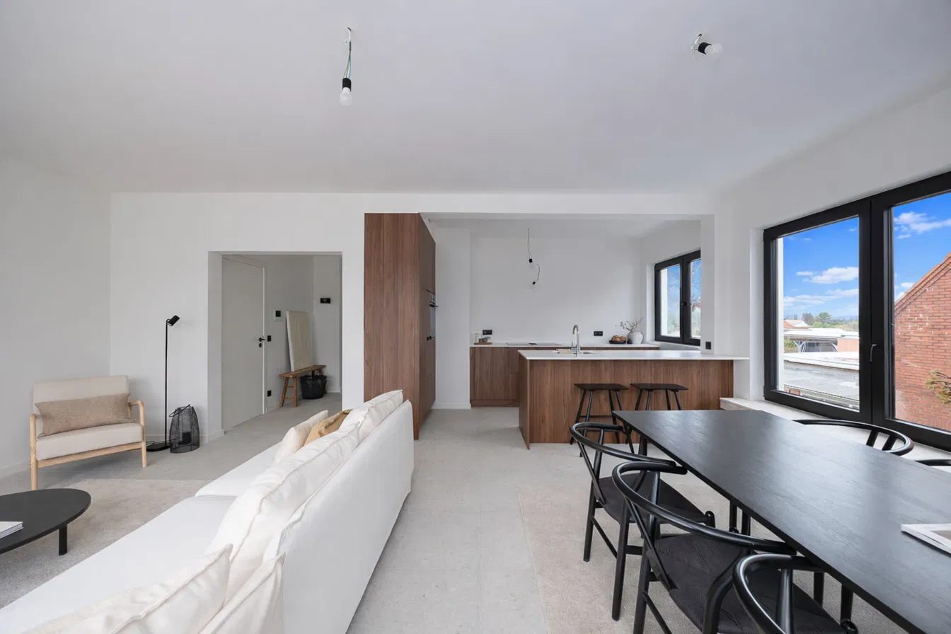 Open leefruimte met zithoek, eettafel en keuken met bar in notenhout in gerenoveerd appartement aan de Heislagsebaan 198 in Brasschaat