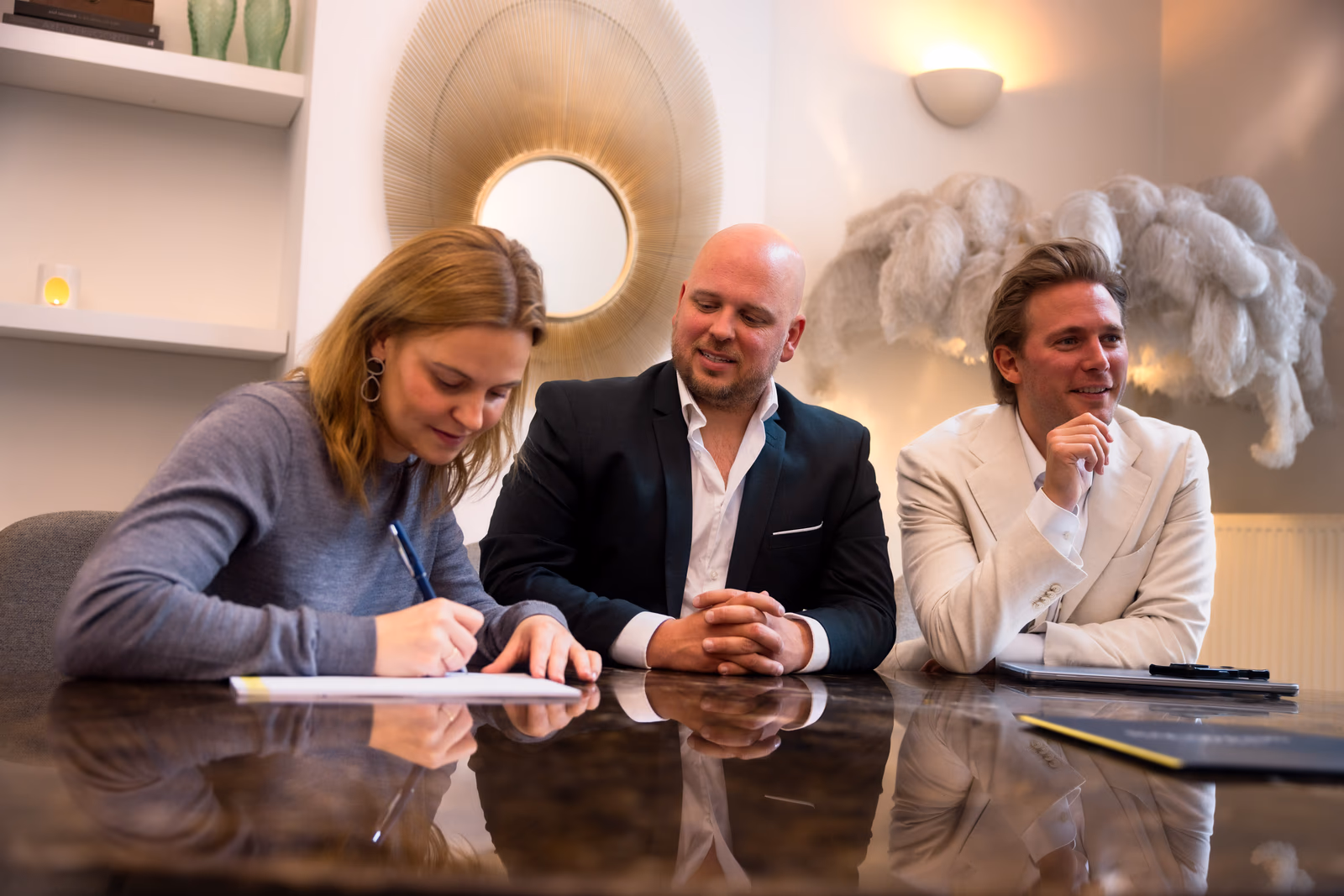 Klant ondertekent een document, begeleid door twee vastgoedadviseurs van Bauwens Vastgoed
